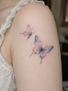 Watercolor style two butterflies upper arm tattoo