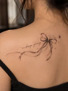 Fine line ribbon bow and lettering upper back tattoo