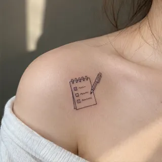 Minimalist fine line notepad and pen collarbone tattoo