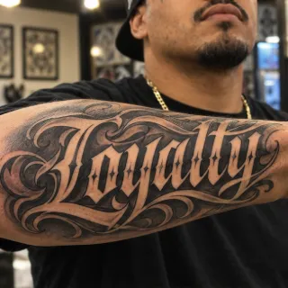 Loyalty lettering with ornate black and grey forearm tattoo