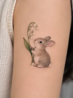 Small realistic rabbit and lily of the valley arm tattoo