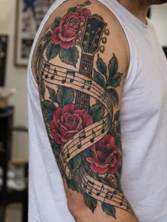 Traditional guitar rose and musical notes upper arm tattoo