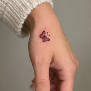 Small red butterfly hand tattoo with fine line details