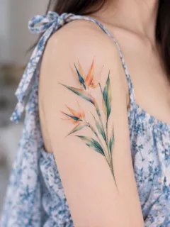 Watercolor bird of paradise flower upper arm tattoo
