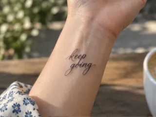 Fine line script keep going lettering wrist tattoo