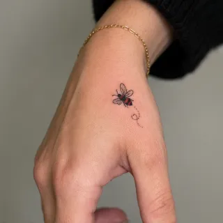 Small fine line bee hand tattoo with red accents